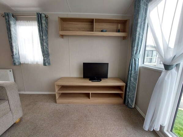 Quarto com televisão sobre um suporte de madeira, um radiador e janela com cortinas.