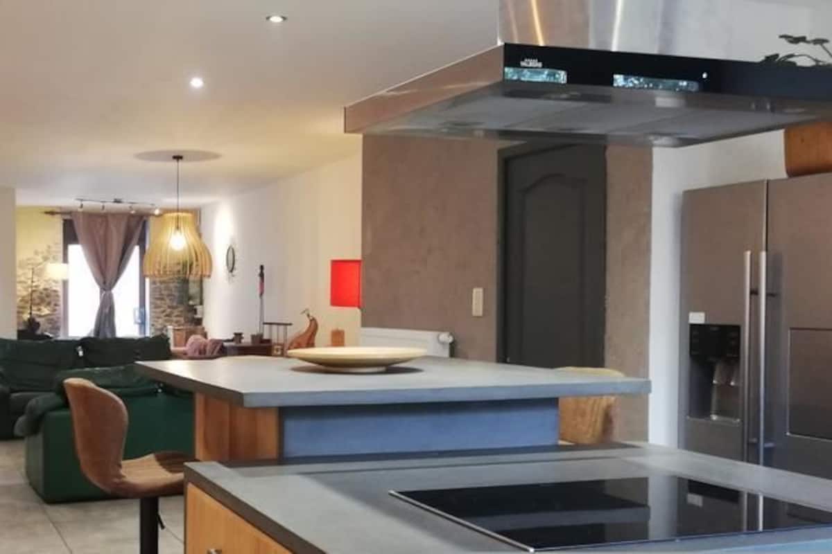A modern kitchen with a central island, a dining area with chairs, and a living room with a sofa.
