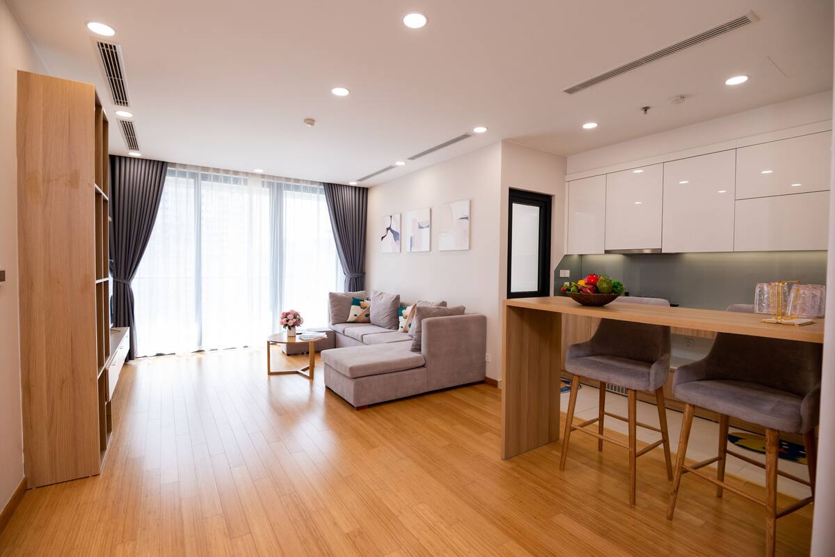 A modern living room with a sofa, a dining table with bar stools, and a kitchen area.