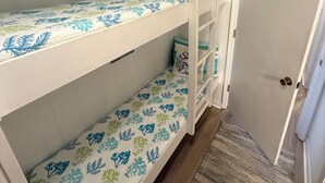 Un llit superposat amb roba de llit de motius florals, una porta blanca amb un senyal damunt i un terra de fusta.