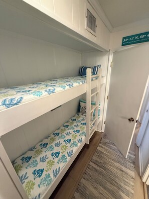 Un letto a castello con biancheria da letto a motivi floreali, una porta bianca con un cartello sopra e un pavimento in legno.