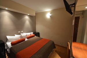 Una habitación de hotel con una cama, mesitas de noche, una silla y una puerta.