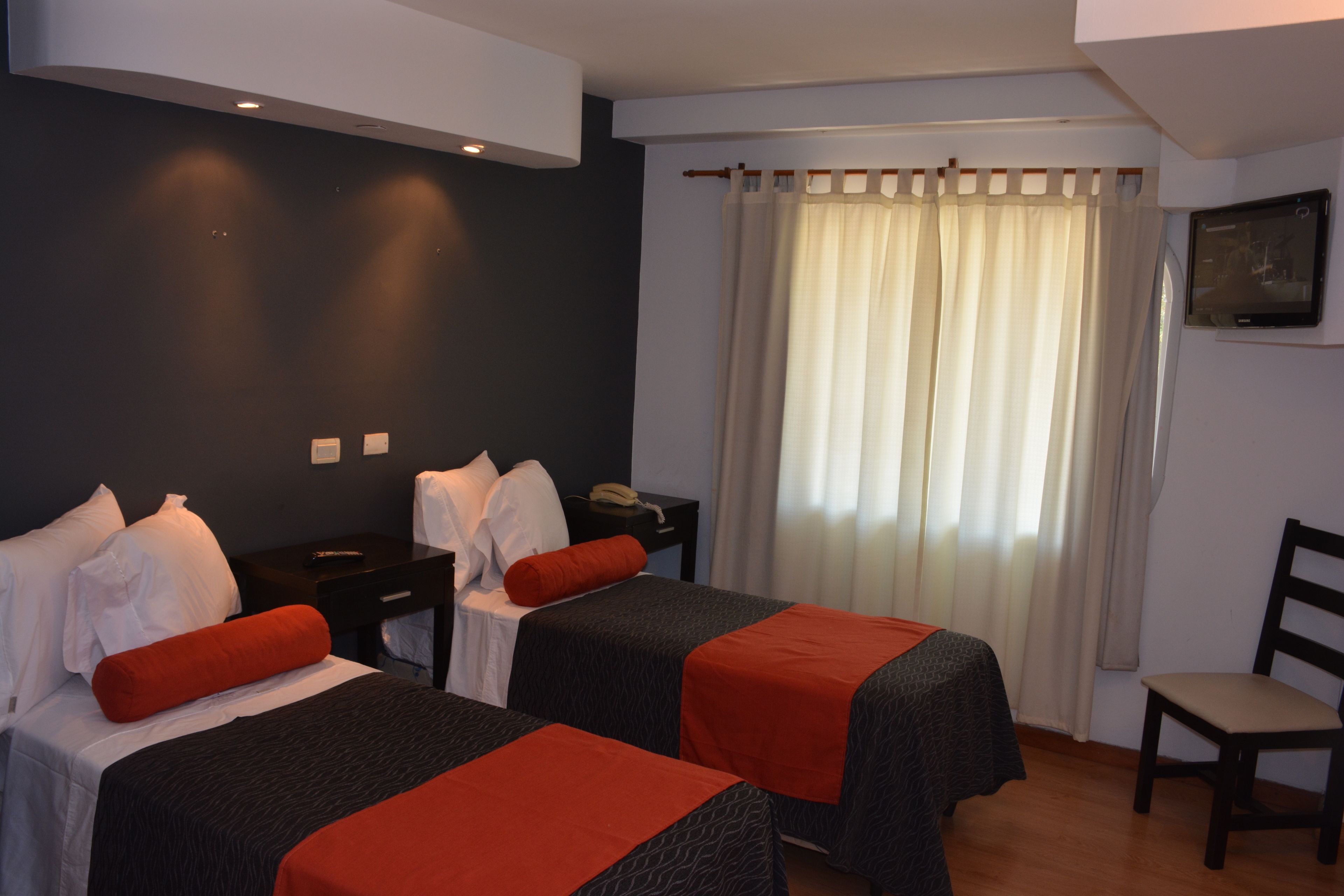 A hotel room with two beds, a desk, a chair, a television, and a window with curtains.