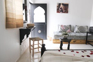 A room with a bed, a sofa, a small table with a plant, a wooden stool, and a black door with a white arch. - Run villa Marine (Marrakech)