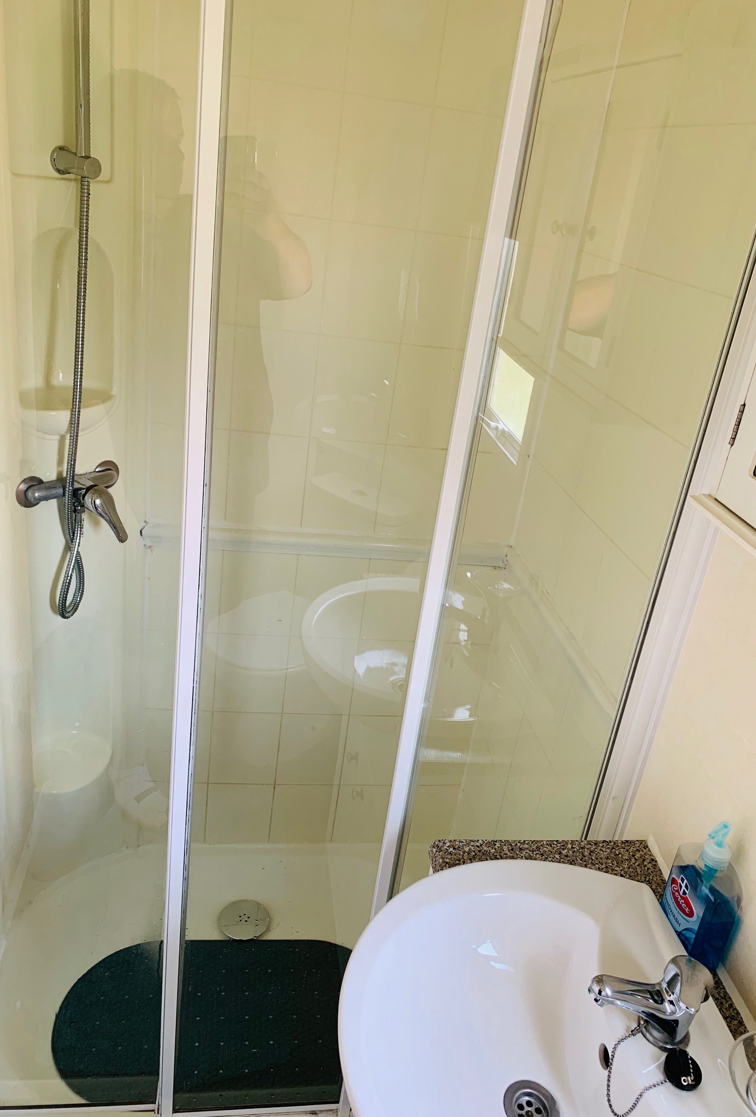 A glass-enclosed shower with a handheld showerhead and a handheld faucet.