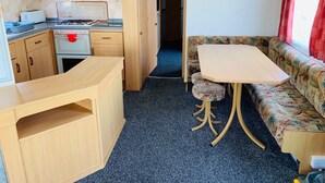 A compact kitchenette with a stove, sink, and cabinets, a small dining table with a bench, and a sofa with a patterned cushion.