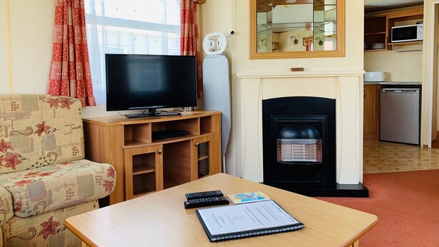 A living room with a television, sofa, coffee table, fireplace, and kitchen area.