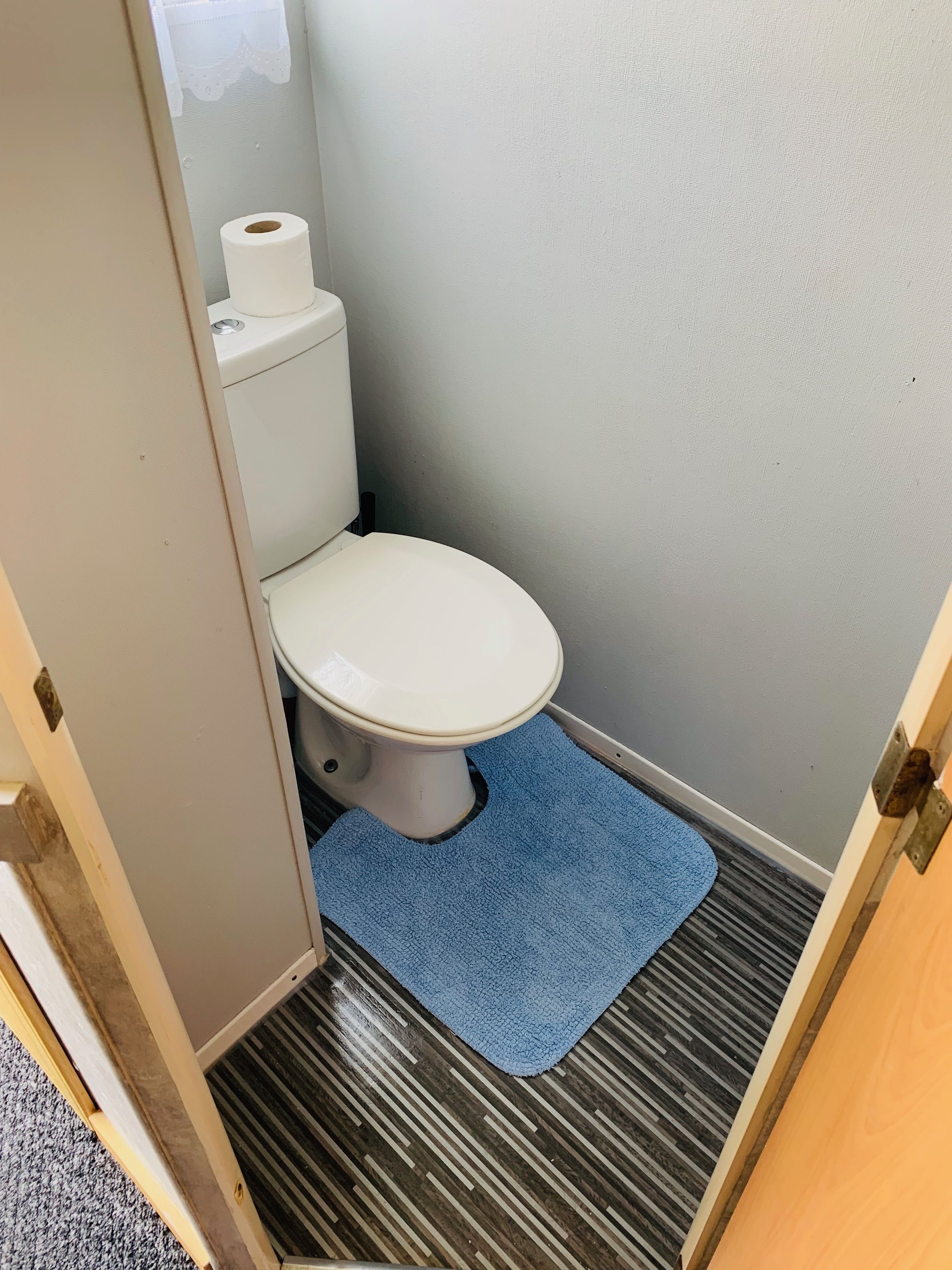 A small bathroom with a toilet, a blue mat, and a striped floor.