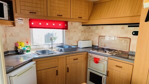 A compact kitchen with wooden cabinets, a sink, a toaster, a stove, and a refrigerator.