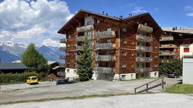 A multi-story wooden building with balconies, a parking area, and a mountain view. - Pracondu 2 401 - OUTDOOR & FUN  apartment 6 pers (Haute-Nendaz)