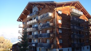 A multi-story wooden building with balconies, likely a hotel or lodging facility, with a mountainous backdrop. - Pracondu 2 401 - OUTDOOR & FUN  apartment 6 pers (Haute-Nendaz)