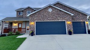 A two-story house with a stone facade, two garage doors, and a small porch with a railing.