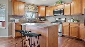 A modern kitchen with wooden cabinets, a central island with bar stools, a microwave, and a stove.