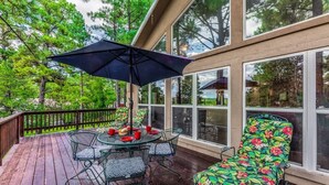 A covered outdoor deck with a table and chairs, surrounded by large windows and a view of trees. - Four Bears Bungalow (Ruidoso)