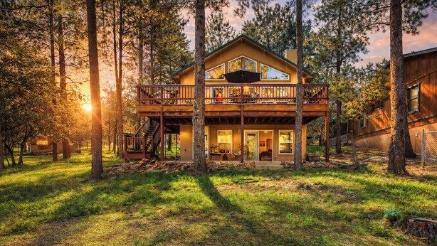 A two-story cabin with a balcony, surrounded by trees and a grassy yard. - Four Bears Bungalow (Ruidoso)