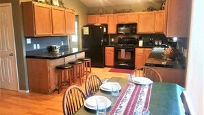 Una cocina con armarios de madera, un refrigerador negro, una estufa y un comedor con una mesa dispuesta para cuatro.