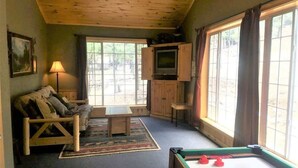 Una habitación acogedora con techo de madera, un sofá, una mesita, un televisor y una mesa de billar.
