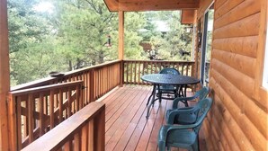 Una terraza de madera con una mesa y sillas, rodeada de árboles.