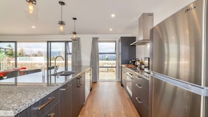 A modern kitchen with a stainless steel refrigerator, wooden flooring, and a large window overlooking a deck. - Lofty Quarters - Hamner Springs Holiday Home (Hanmer Springs)