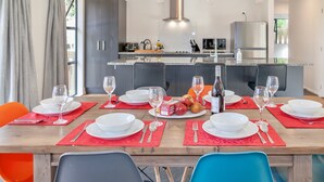A dining area with a wooden table set for six, red placemats, white plates, and clear glassware. - Lofty Quarters - Hamner Springs Holiday Home (Hanmer Springs)