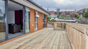 A wooden deck with glass doors leading to a room with a sofa and a television. - Lofty Quarters - Hamner Springs Holiday Home (Hanmer Springs)