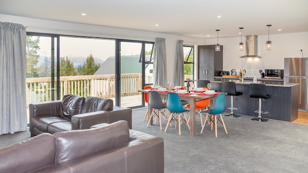A modern living room with a sofa, dining area with chairs, and a kitchen with a bar. - Lofty Quarters - Hamner Springs Holiday Home (Hanmer Springs)