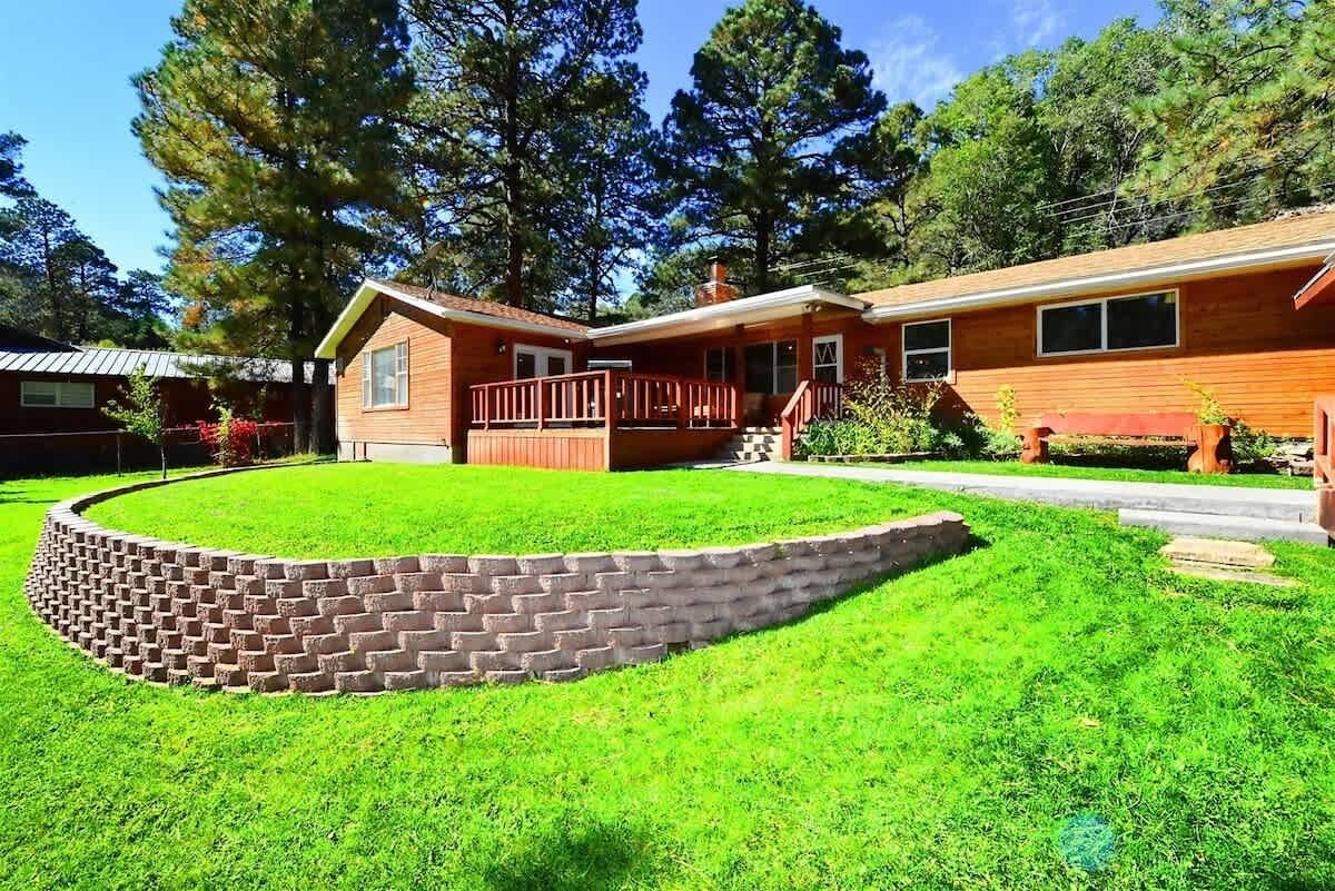 A two-story house with a front deck, a brick retaining wall, and a well-maintained lawn.