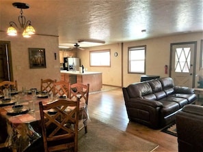 A spacious living area with a dining table set for four, a leather sofa, and a kitchen in the background. - Rivers Edge Cabin (Ruidoso)