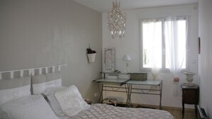 Ein Schlafzimmer mit Bett, Schreibtisch, Stuhl, einer Kristallleuchtre und einem Fenster mit Vorhängen.