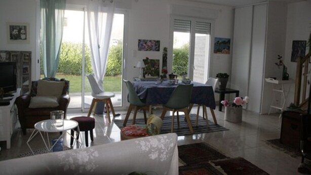 Ein Wohnzimmer mit einer Couch, einem Couchtisch und einem Essbereich mit Stühlen und einem Tisch. Es gibt einen Fernseher, eine Pflanze und Kunstwerke an den Wänden.