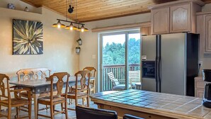 A kitchen with a dining table, chairs, a refrigerator, and a view of the outdoors. - Spacious Mountain-Views with Game Room + Fireplace (Alto)