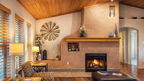 A cozy living room with a fireplace, wooden ceiling, and a decorative wall piece. - Spacious Mountain-Views with Game Room + Fireplace (Alto)