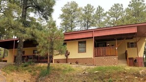 A single-story building with a red roof and beige siding, surrounded by pine trees. - Papa Bears Cabin (Ruidoso)