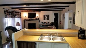 A compact kitchen with a double sink, wooden countertop, and a fireplace in the background. - Papa Bears Cabin (Ruidoso)