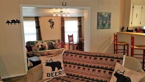 A cozy living room with a sofa, a bear-themed pillow, and a chair. - Papa Bears Cabin (Ruidoso)