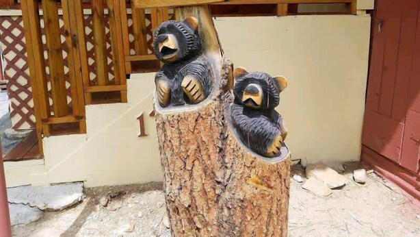 A wooden sign with the word "WELCOME" above two bear sculptures on a tree stump. - Papa Bears Cabin (Ruidoso)