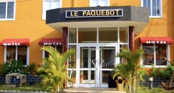 A hotel named "Le Paquebot" with a glass entrance, red awnings, and palm trees in the foreground. - Hôtel Le Paquebot - Airport Paquebot hotel (Cotonou)