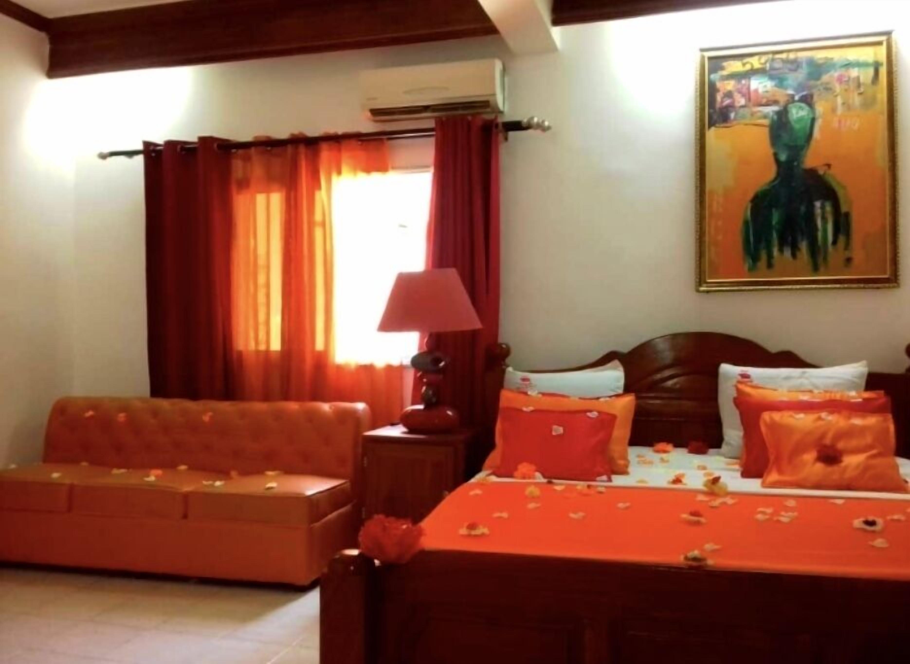 A hotel room with a bed, a sofa, a lamp, and a painting on the wall.