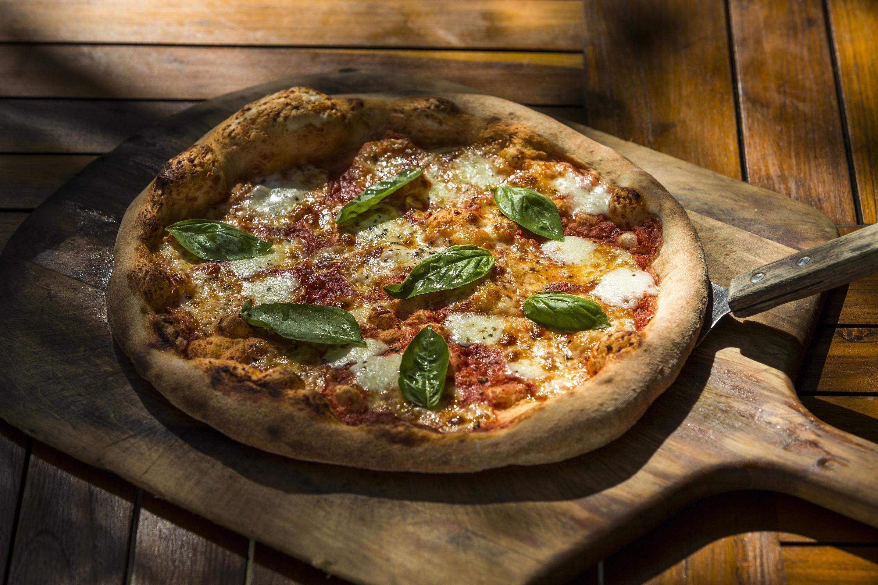 A pizza on a wooden board with a pizza cutter.