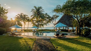 A pool area with lounge chairs and umbrellas, surrounded by palm trees and a view of the ocean. - Turtle Inn by Francis Ford Coppola (Placencia)
