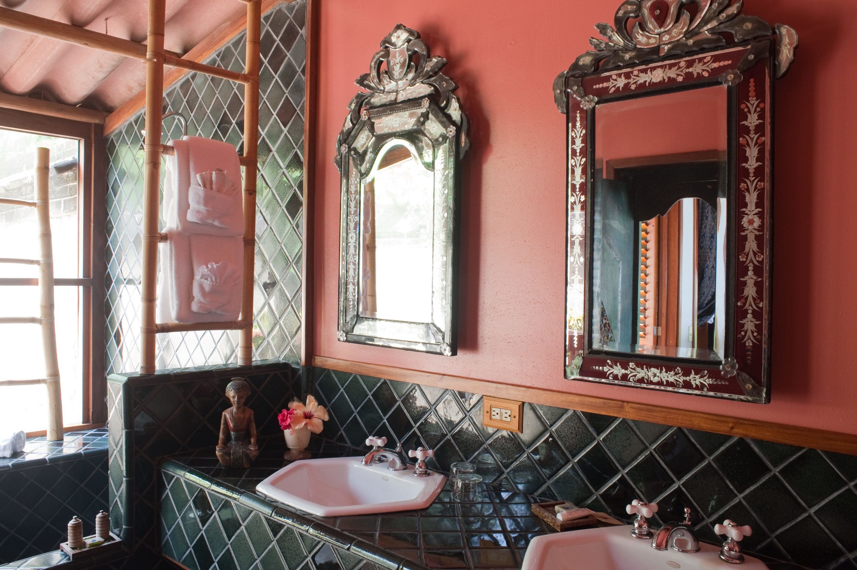 Un baño con tocador, dos espejos, lavabo y una estatua decorativa de Buda.