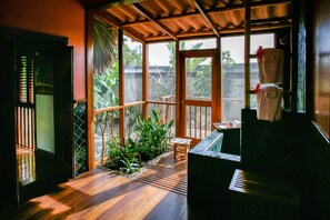 A wooden deck with a small table and chairs, surrounded by plants and a view of the outdoors.