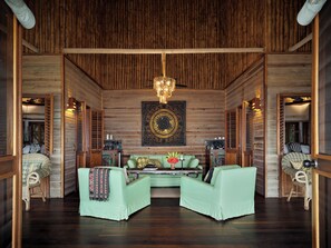 A room with a wooden ceiling, a chandelier, a green sofa, a table with decorative items, and a wall with a circular pattern.