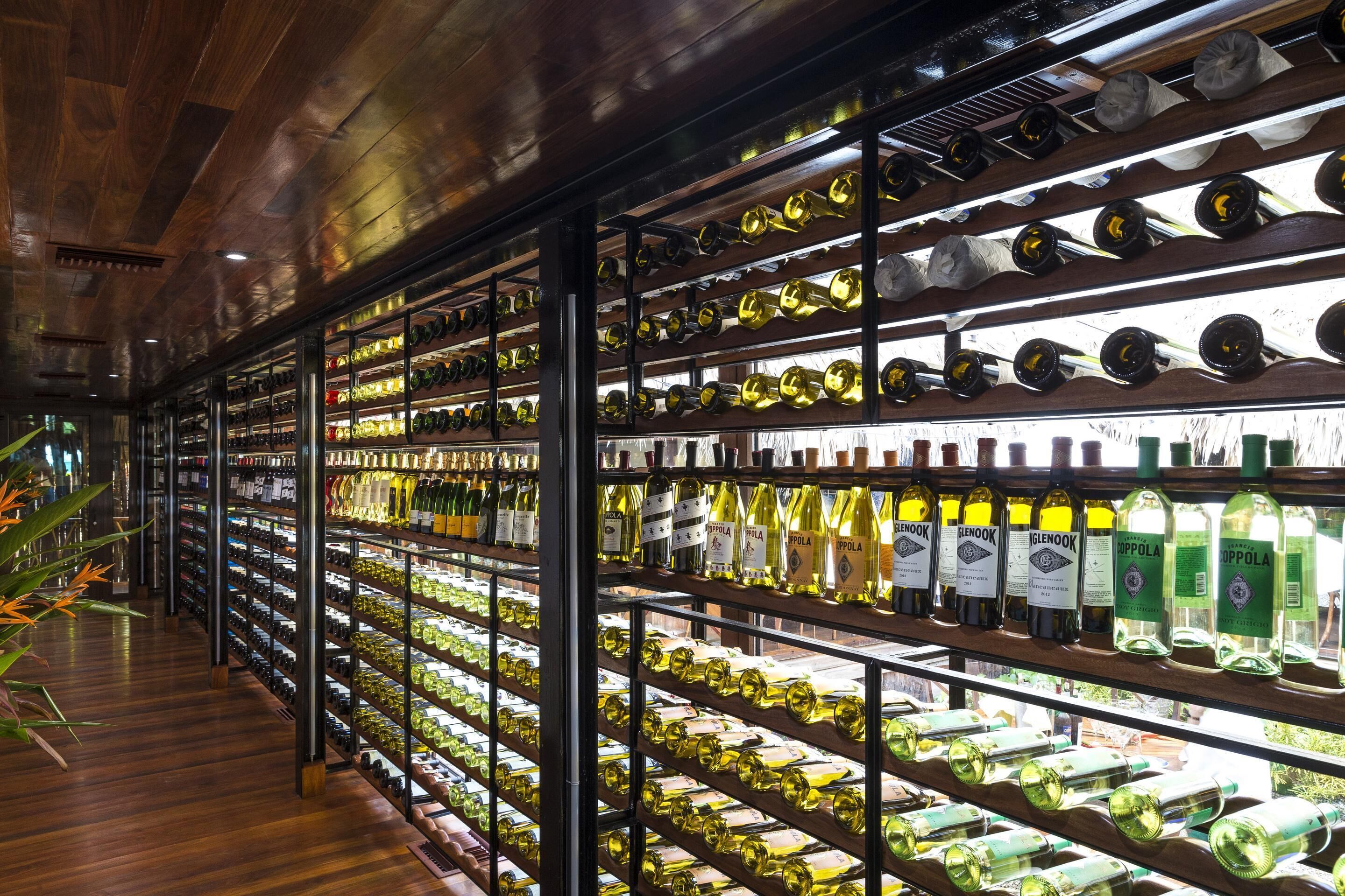 Una bodega con estantes llenos de botellas de vino, piso de madera y estanterías metálicas.