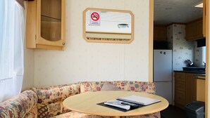A cozy RV interior with a round table, patterned sofa, wooden cabinets, a kitchen area, and a 'No Smoking' sign. - Golden Sands Caravan Hire (Skegness)