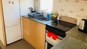 A compact kitchen with wooden cabinets, a white refrigerator, a microwave, a sink, and a stove. - Golden Sands Caravan Hire (Skegness)