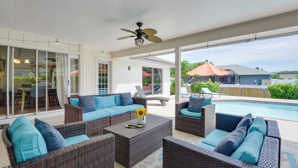 A covered outdoor area with wicker furniture, a ceiling fan, and a view of a swimming pool.
