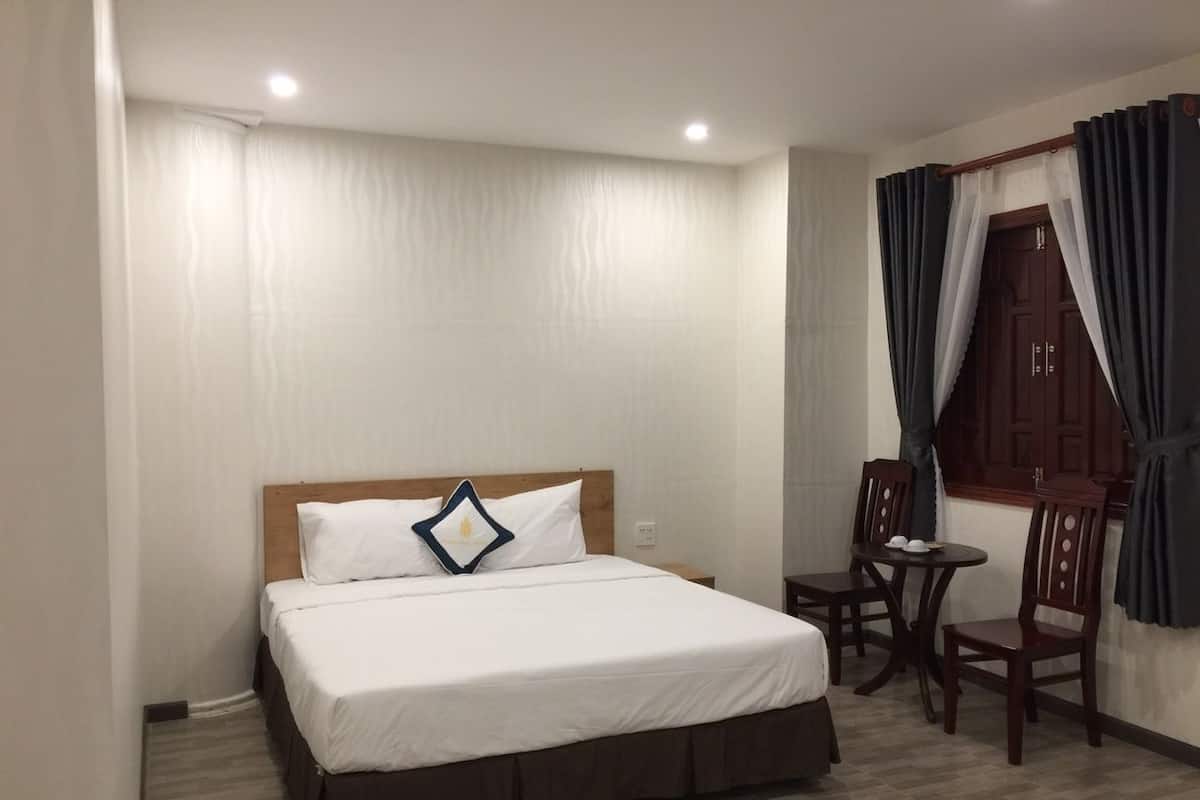Ein Hotelzimmer mit einem Einzelbett, einem kleinen Tisch mit zwei Stühlen und einer Holztür mit Vorhängen.
