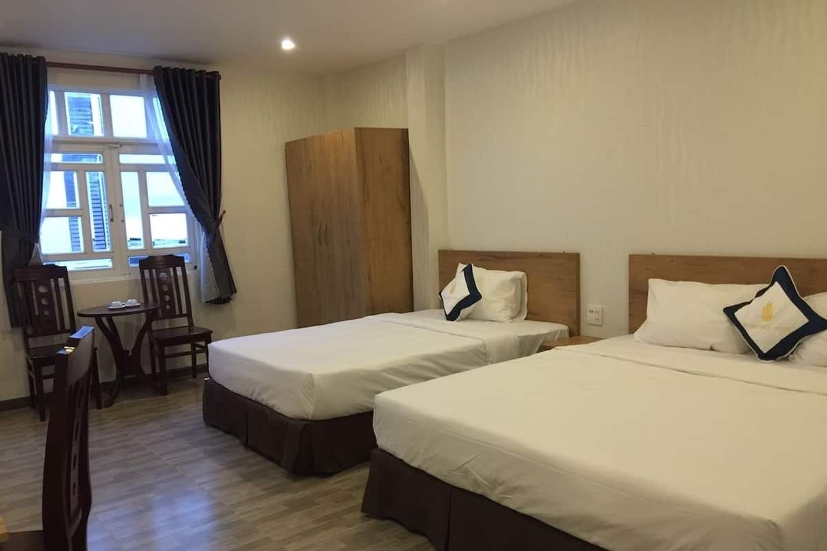 Ein Hotelzimmer mit zwei Betten, einem Holzschrank, einem kleinen Tisch mit Stühlen und einem Fenster mit Vorhängen.