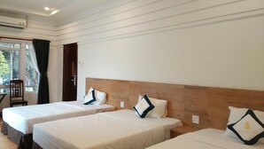 Une chambre d’hôtel avec trois lits simples, une tête de lit en bois et une fenêtre avec des rideaux.